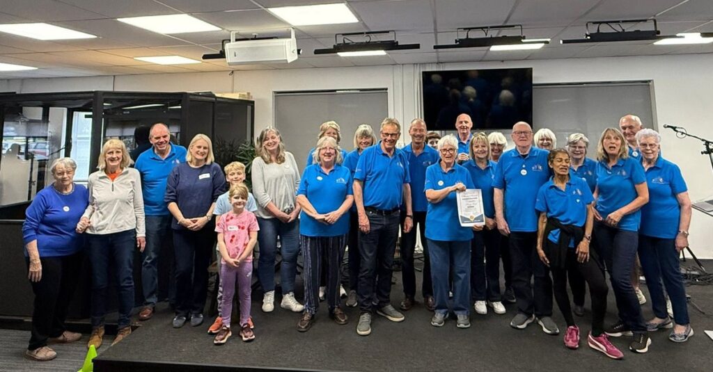 The Dementia Sings Out volunteer team in blue polo shirts with the Wellingborough Town Council Citizens Award certificate