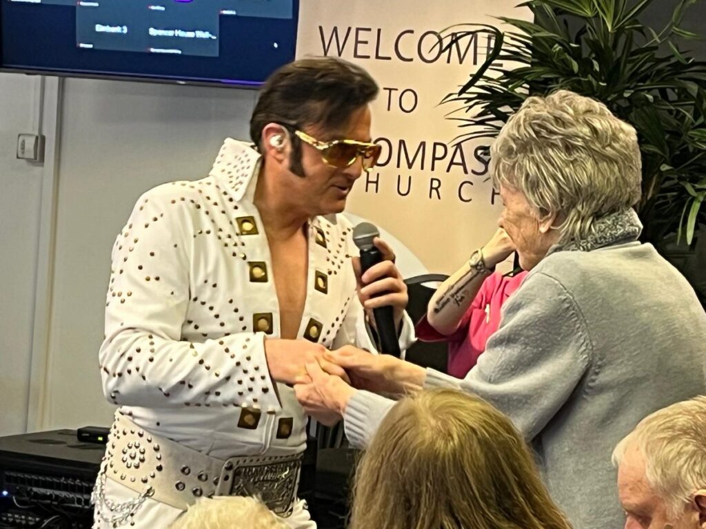 An Elvis tribute act in a white studded jumpsuit singing to a DSO member at Compass Church