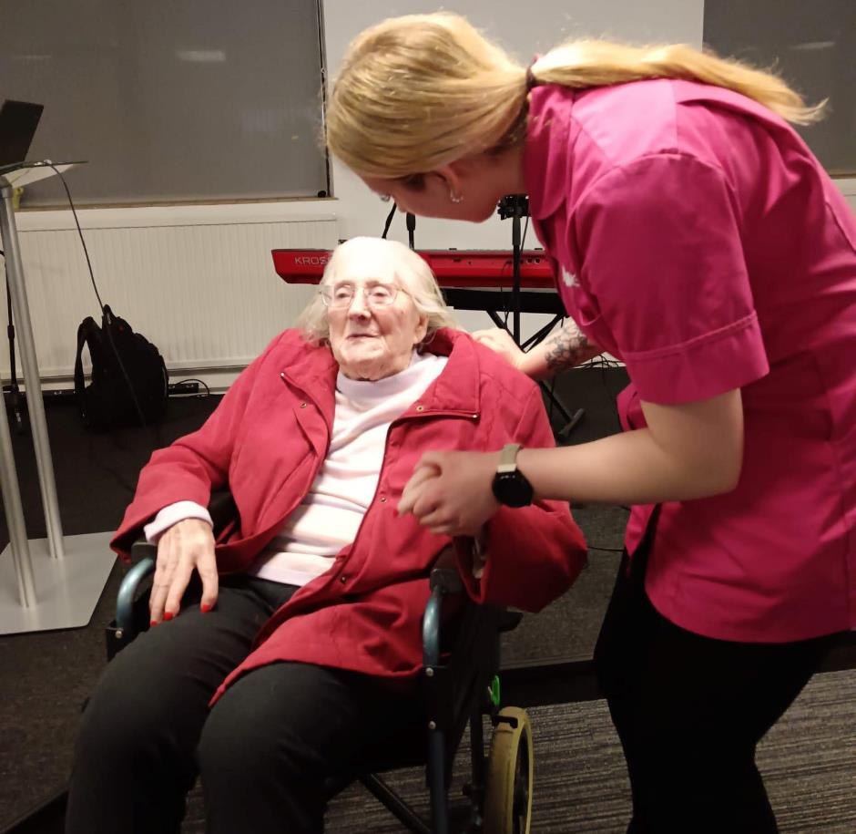 A carer in a pink uniform holding hands with Hazel, a DSO attendee, at her 100th birthday celebration