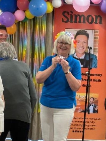 Kathryn in a blue Dementia Sings Out polo shirt holding up her silver medal at the Overstone House Summer Festival