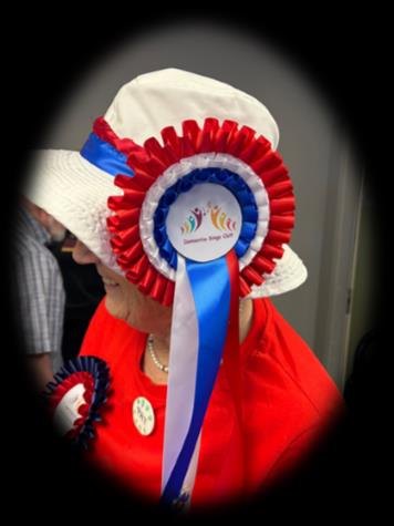 A DSO member wearing a white hat with a large red, white and blue Dementia Sings Out rosette