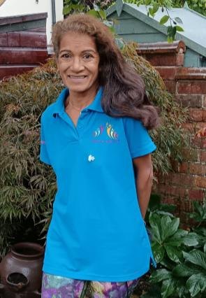 Lisiane Cecile-Sims, a DSO volunteer, standing in a turquoise Dementia Sings Out polo shirt in a garden